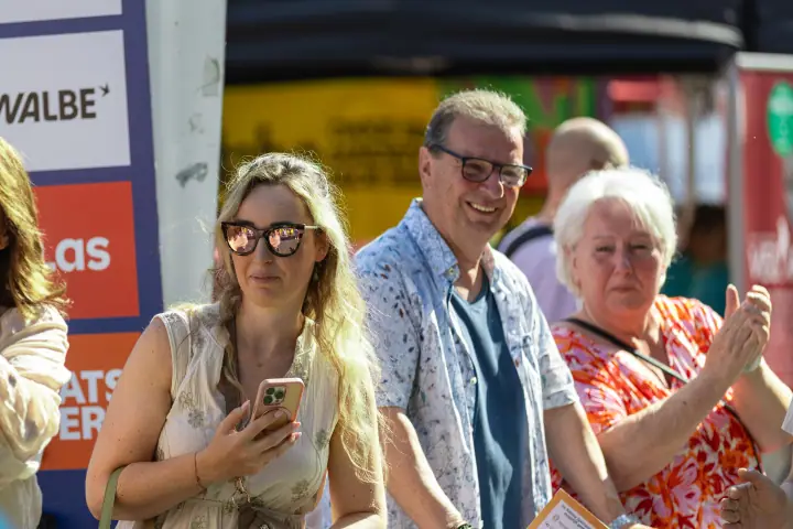 Lachende toeschouwers langs het parcours, een vrouw met telefoon en een applaudisserende dame