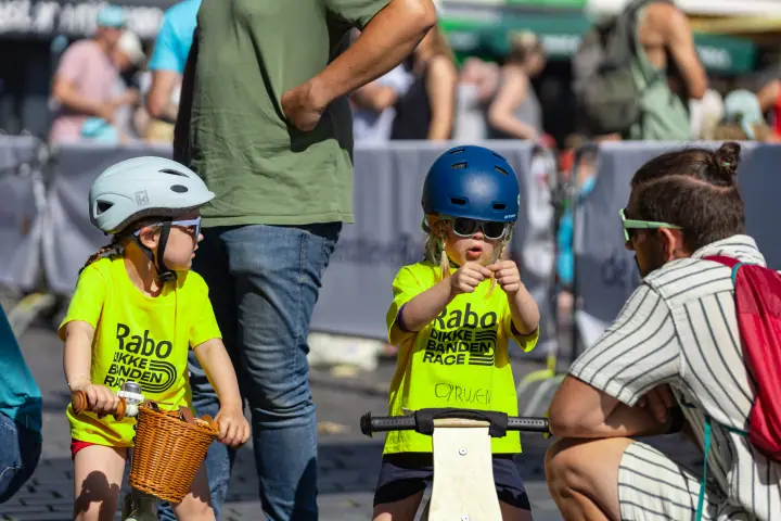 Kleine kinderen op loopfietsen in gele shirts van de Rabo Dikke Banden Race, met een begeleider ernaast