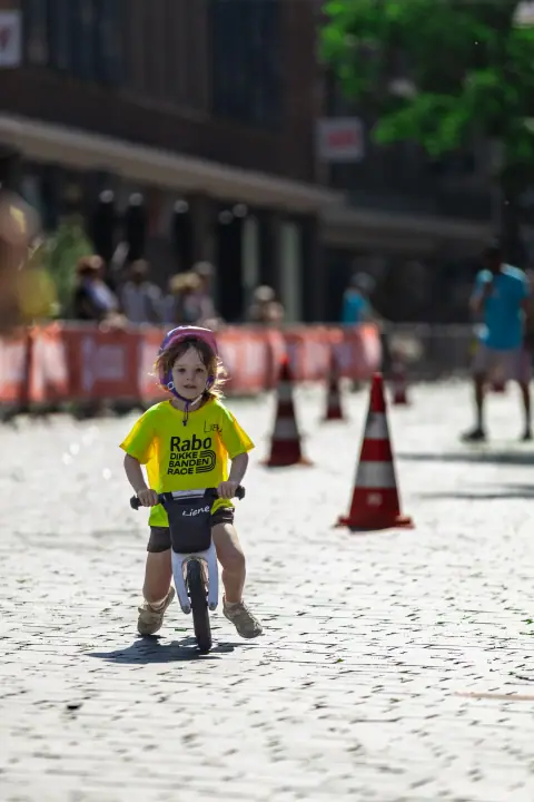 Klein kind op een loopfiets rijdt geconcentreerd tussen de pionnen tijdens de Rabo Dikke Banden Race
