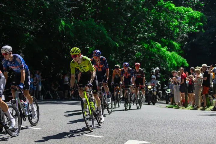 Renners nemen een zonnige bocht, langs toeschouwers aan de rand van het bos