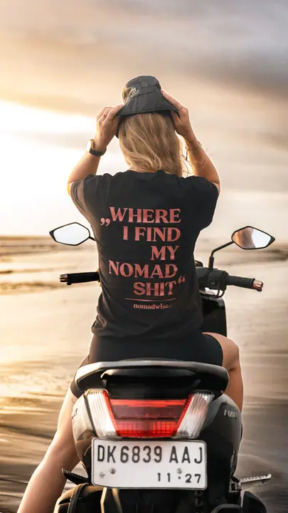 Met beide handen op haar vissershoedje zit ze op de scooter, de roze print op haar rug in beeld.