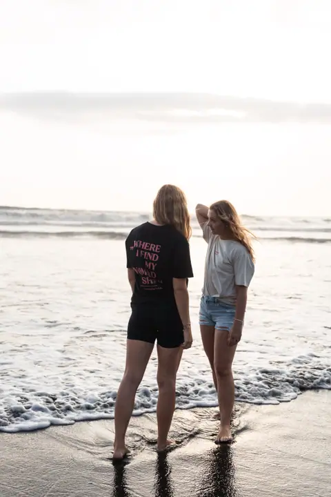 Twee vrouwen in de schuimende branding, de een strijkt door haar haar, de ander toont de rugprint.