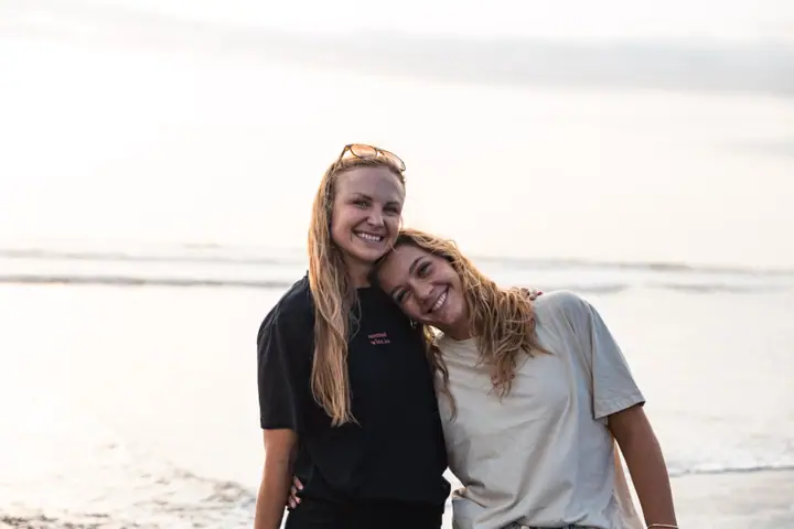 Brandingfotografie voor Nomadwise, twee vrouwen leunen lachend tegen elkaar aan op het strand.