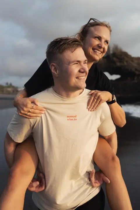 Close-up van een vrouw die lachend op de rug zit van een man in een beige nomadwise.io shirt.