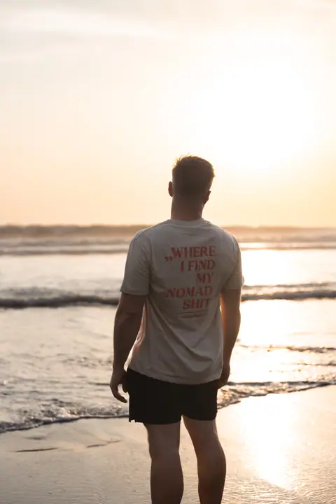 Man in beige Nomadwise shirt staat met zijn rug naar de camera in het gouden avondlicht aan zee.
