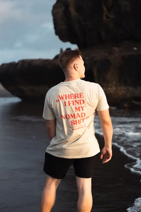 De beige shirtprint scherp in beeld terwijl de man opzij kijkt, een donkere rots op de achtergrond.