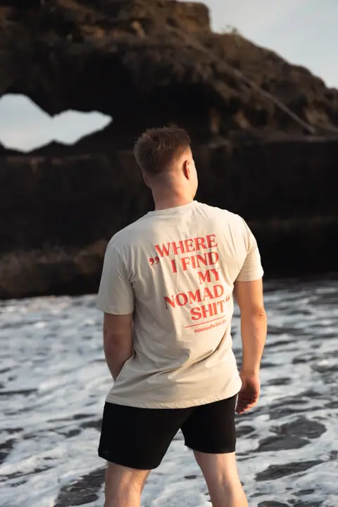 Man in de branding voor een rotsboog, op zijn rug de rode tekst Where I find my nomad shit.