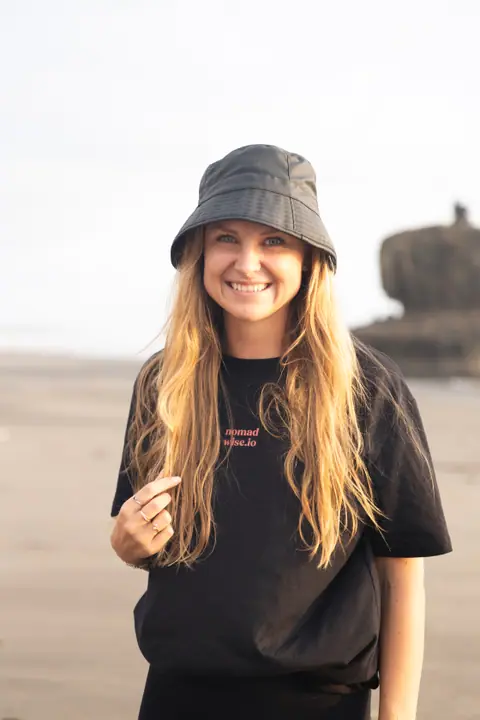 Portret van een lachende vrouw met vissershoedje en lang blond haar in een zwart Nomadwise shirt.