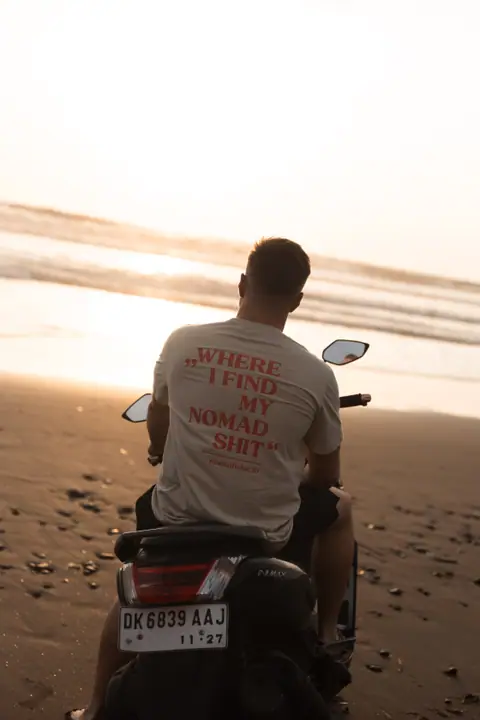 Een man op een scooter aan het strand kijkt uit over zee terwijl de zon ondergaat.