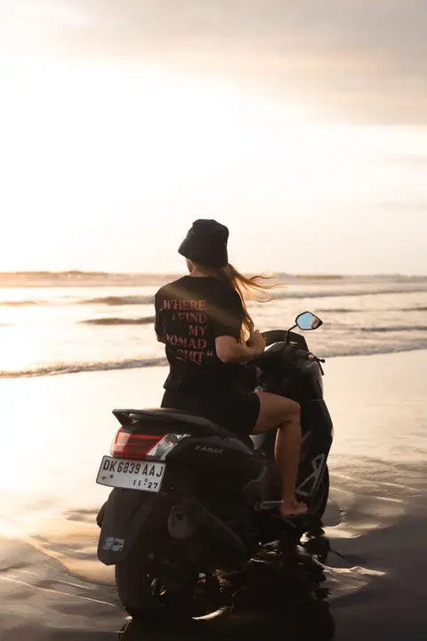 Haar haar wappert in de wind terwijl ze vanaf de scooter uitkijkt over het natte strand.