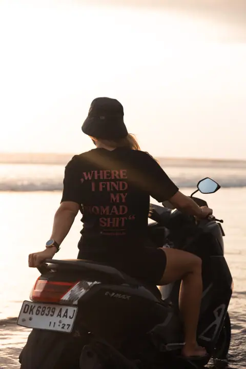 Productfoto in sfeer, de print op een zwart Nomadwise shirt van een vrouw op een scooter in tegenlicht.
