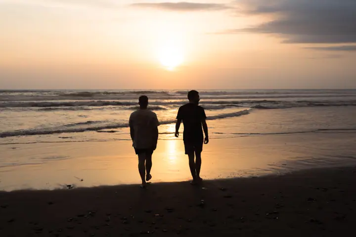 Twee silhouetten lopen naar de golven terwijl de zon laag boven zee hangt.