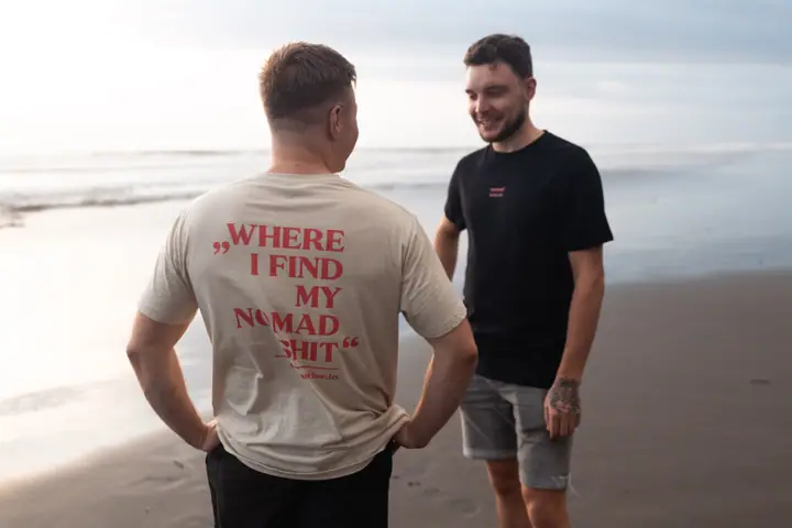 Twee mannen in gesprek op het strand, een met de handen in de zij en de slogan op zijn rug.
