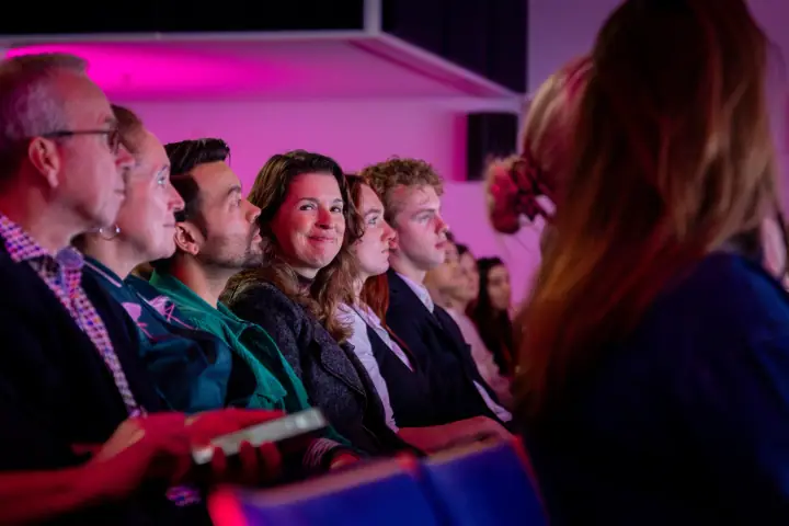 Publiek op de Startup F*ckup Night in Nijmegen, een vrouw in het midden glimlacht naar het podium