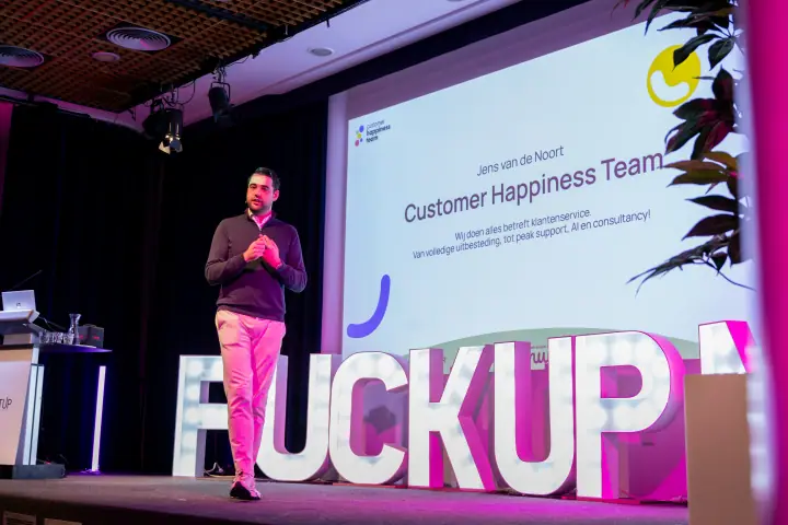 Spreker van Customer Happiness Team vertelt zijn verhaal, van onderaf gefotografeerd achter de lichtletters