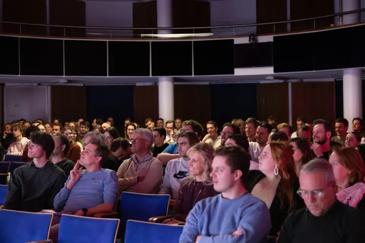Afgeladen zaal met rijen bezoekers die gespannen naar het podium kijken