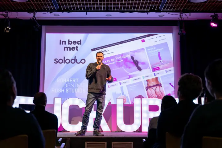 Spreker praat de zaal toe met een webshop op de slide achter zich, het publiek in silhouet vooraan