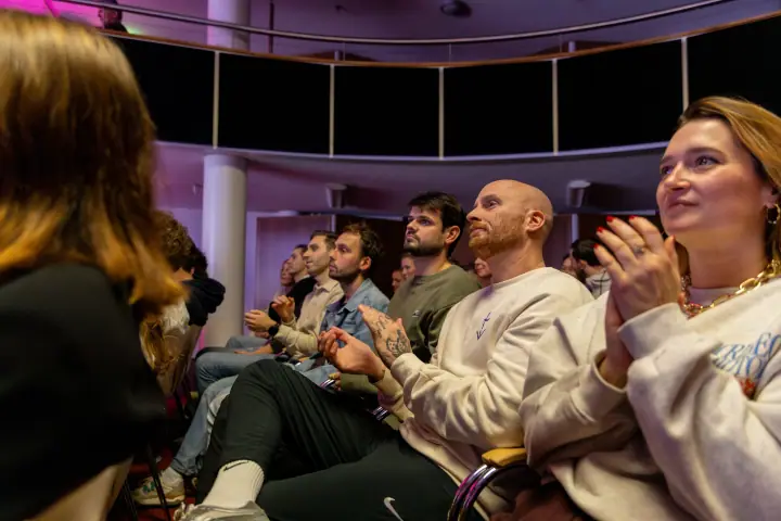 Bezoekers applaudisseren na een talk, vooraan een vrouw met rode nagels en een gouden ketting