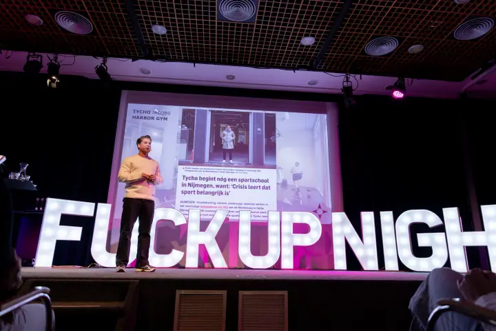 Spreker in kikkerperspectief, staand voor zijn slide en de verlichte letters van F*ckup Night