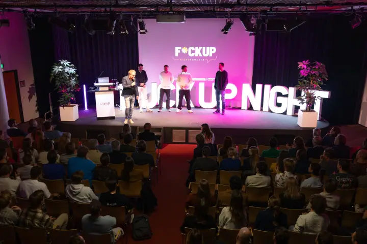 Overzicht van zaal en podium in Nijmegen, waar de sprekers samen voor een volle zaal staan