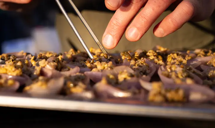 Met een pincet wordt de topping geschikt op een bakplaat vol kleine roze hapjes