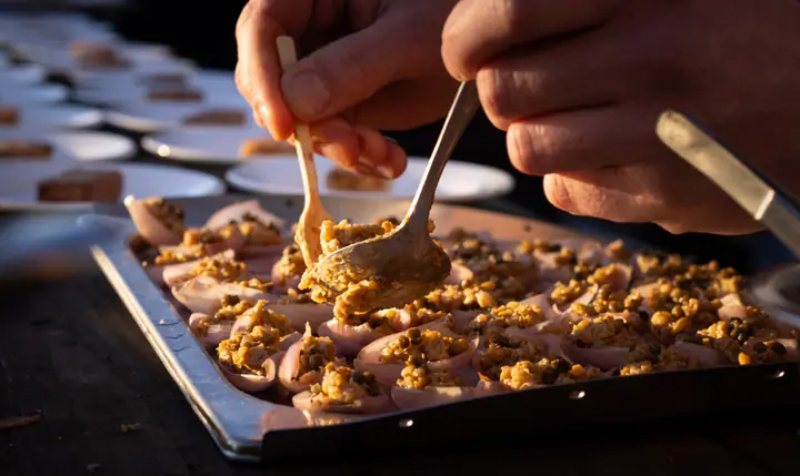 Twee lepels scheppen een kruimeltopping op de hapjes, in het warme licht van de lage zon