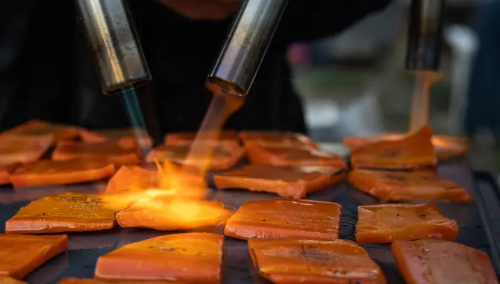 Twee branders schroeien de oranje plakken, de vlam slaat zichtbaar over het product