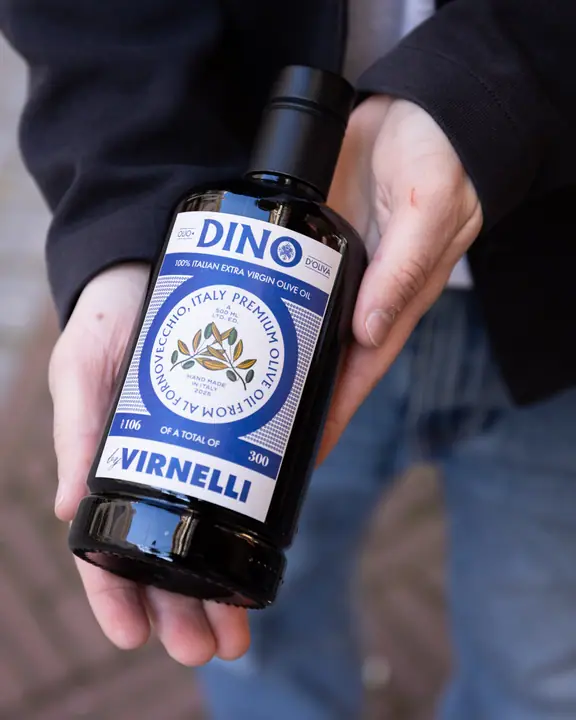 Fles DINO olijfolie van Virnelli in twee handen, met het blauwe etiket goed leesbaar