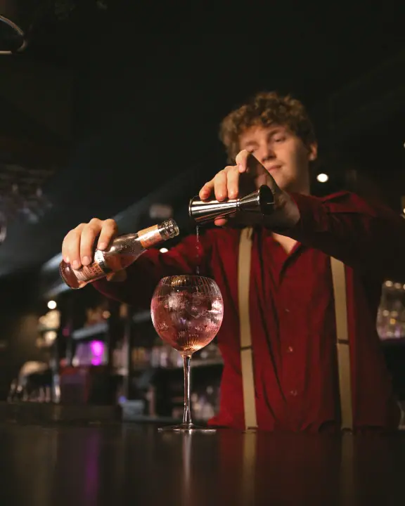Lage hoek op een bartender die een roze longdrink opbouwt in een groot ballonglas