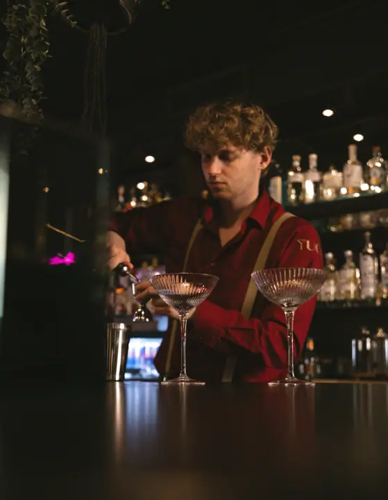 Bartender van YUCA Cocktailbar schenkt een cocktail in twee geslepen coupeglazen
