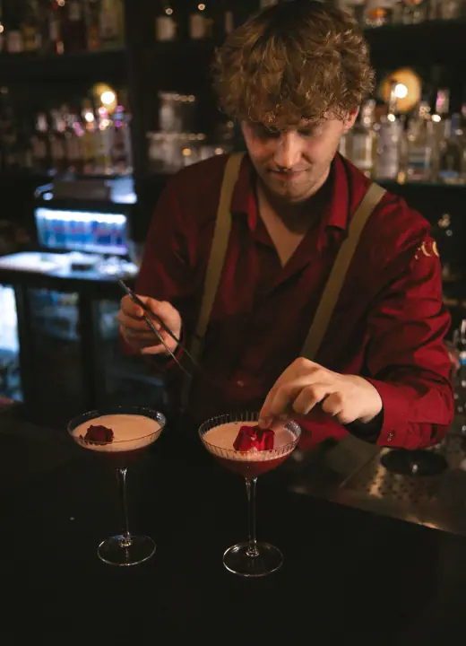 Met een pincet legt de bartender een rode garnering op twee schuimige cocktails