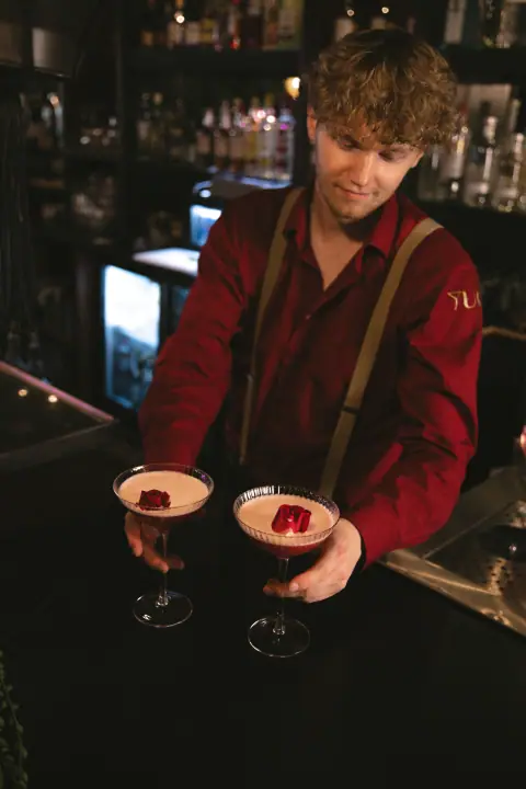 Bartender schuift twee afgewerkte rode cocktails met schuimkraag over de bar