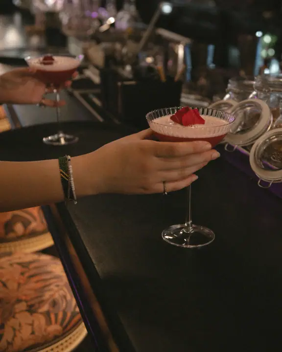 Een rode cocktail met schuimkraag wordt over de donkere bar aangereikt