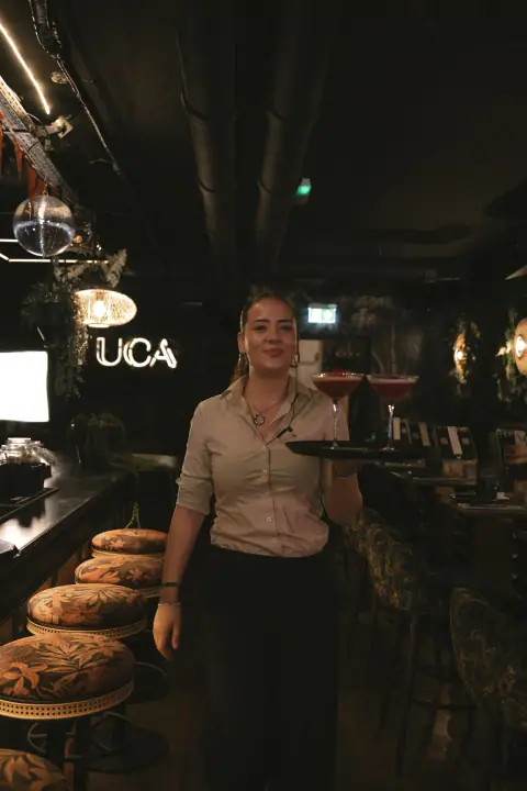 Medewerker loopt met een dienblad cocktails door YUCA in Nijmegen, langs het neonbord en de discobal