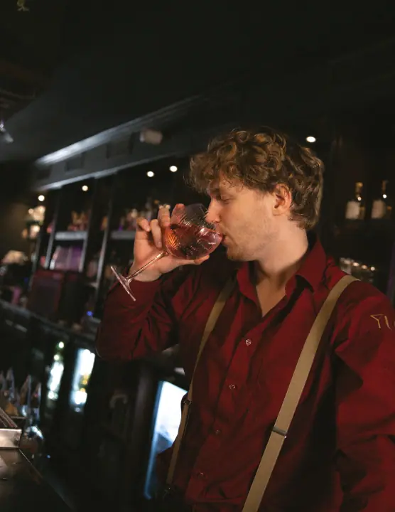 Bartender proeft een roze drankje uit een ballonglas achter de bar