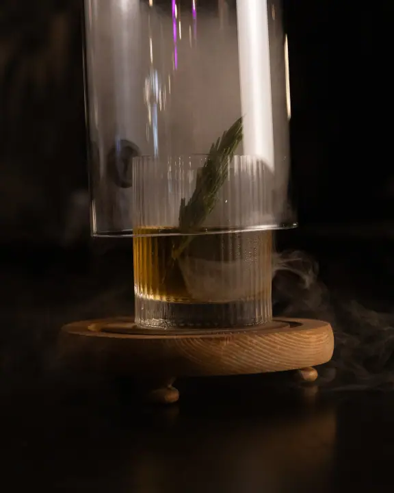 De stolp gaat omhoog en de rook kringelt weg van een cocktail met rozemarijn