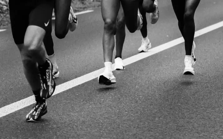 Zwart-wit close-up van benen en hardloopschoenen van een groep lopers op het asfalt