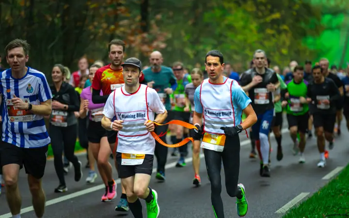 Twee lopers in hesjes van Running Blind, met elkaar verbonden door een oranje koord