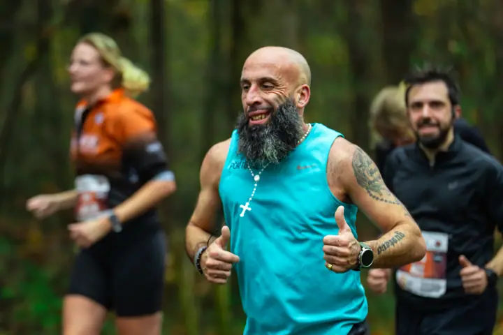 Kale loper met volle baard in een turquoise hemd steekt twee duimen op tussen de bomen