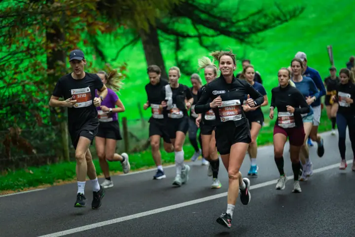 Loopsters in zwarte outfits rennen samen over de weg, de voorste met een brede lach